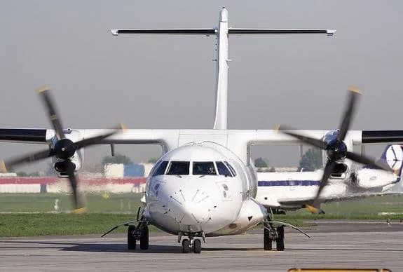 A white turboprop aircraft on the runway with spinning propellers.