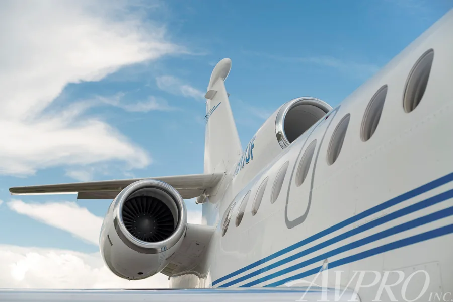 An upward-angled view of the rear fuselage, engines, and tail of the Dassault Falcon 900EX, N917JF, against a blue sky.
