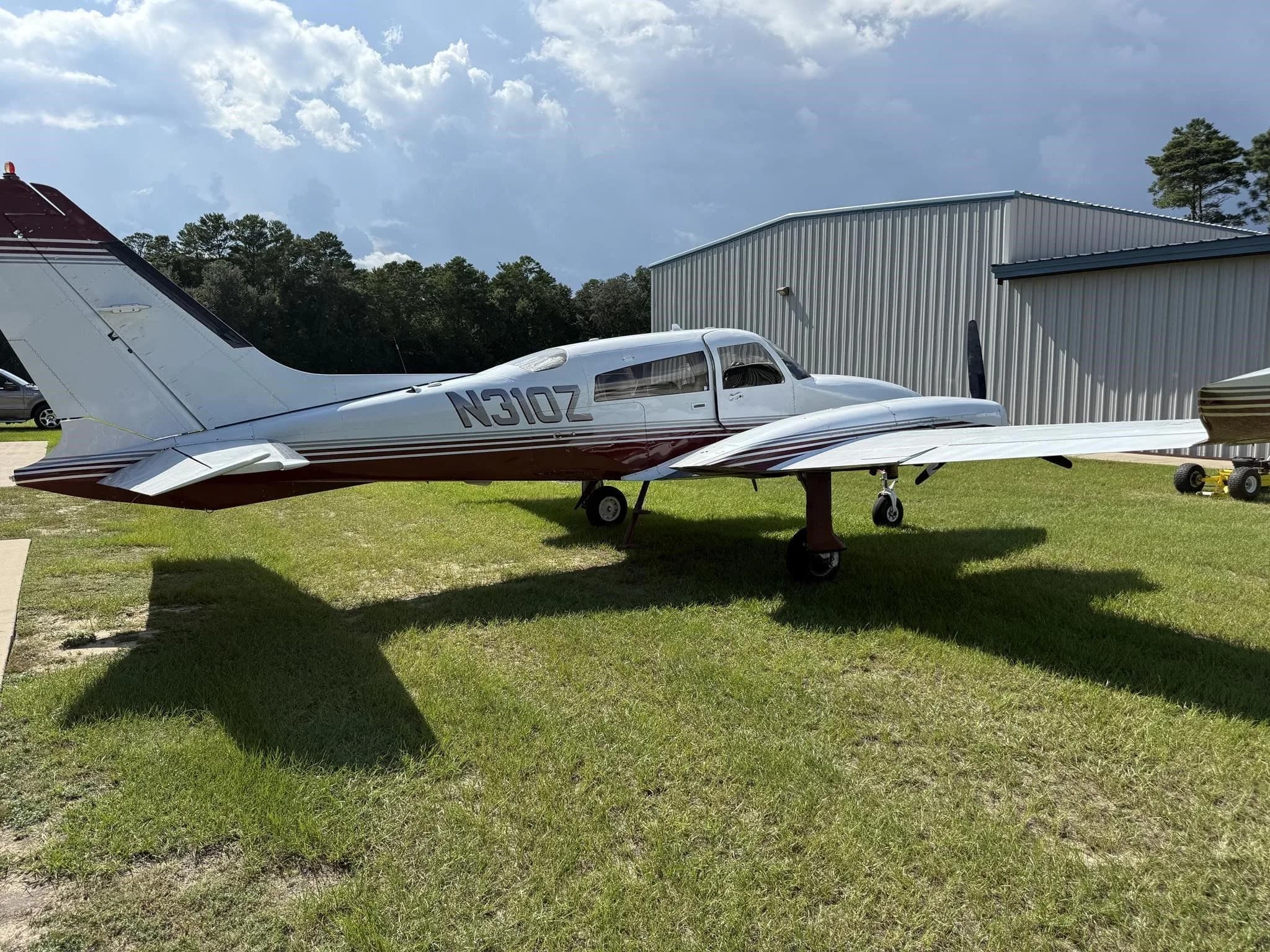 Side-left view of a white and red twin-engine aircraft (N310Z) parked on grass next to a hangar.