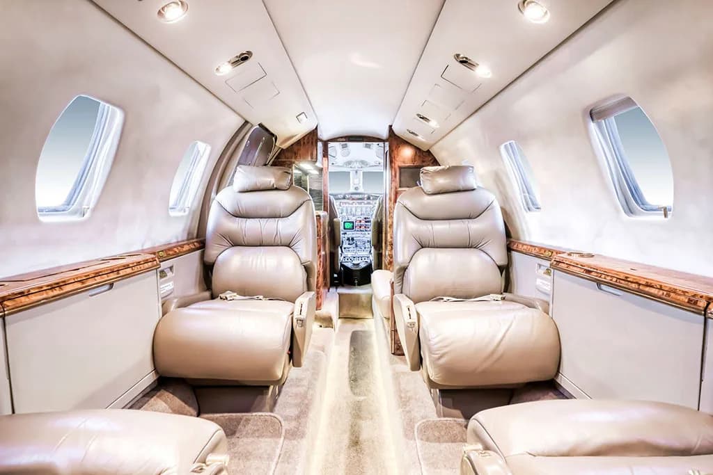 The private jet cabin interior with tan leather seats, looking forward towards the cockpit.