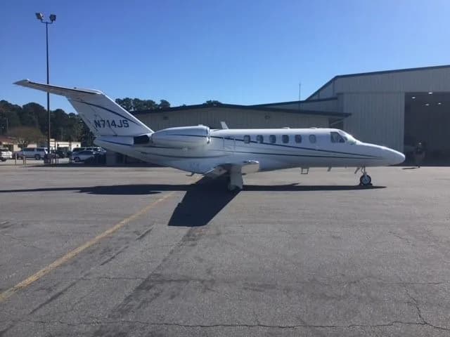 A white Cessna Citation CJ1+ aircraft with registration N714JS parked on the tarmac in front of a hangar.