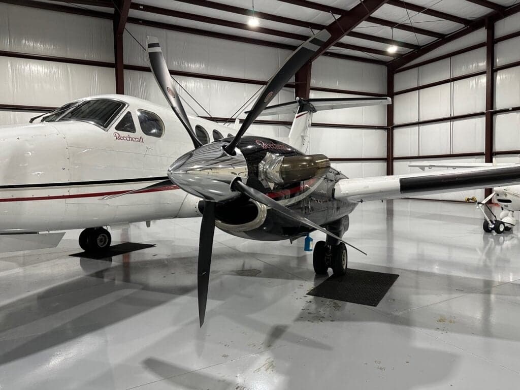 A close-up view of the right engine and propeller of a white Beechcraft King Air in a hangar.