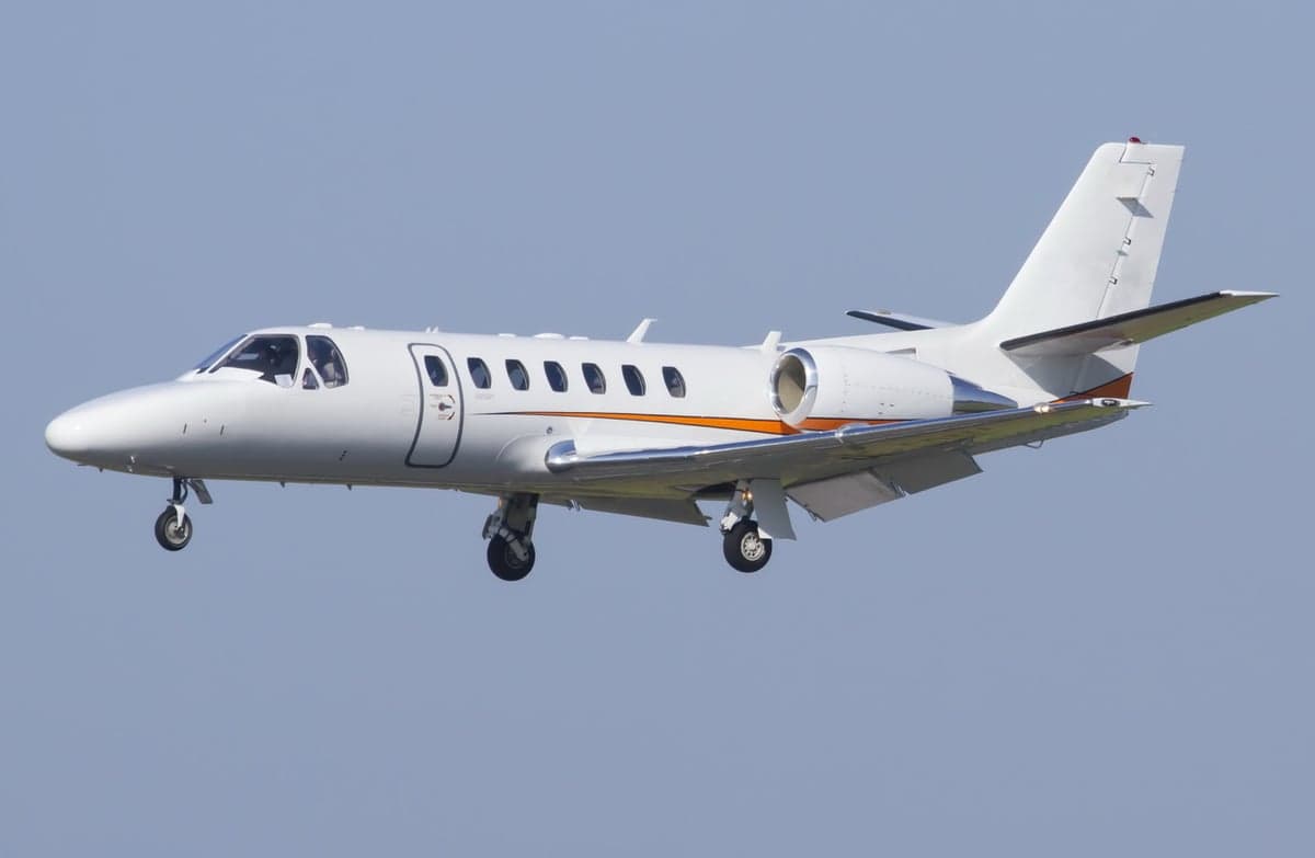 A white jet aircraft is shown in flight against a blue sky.