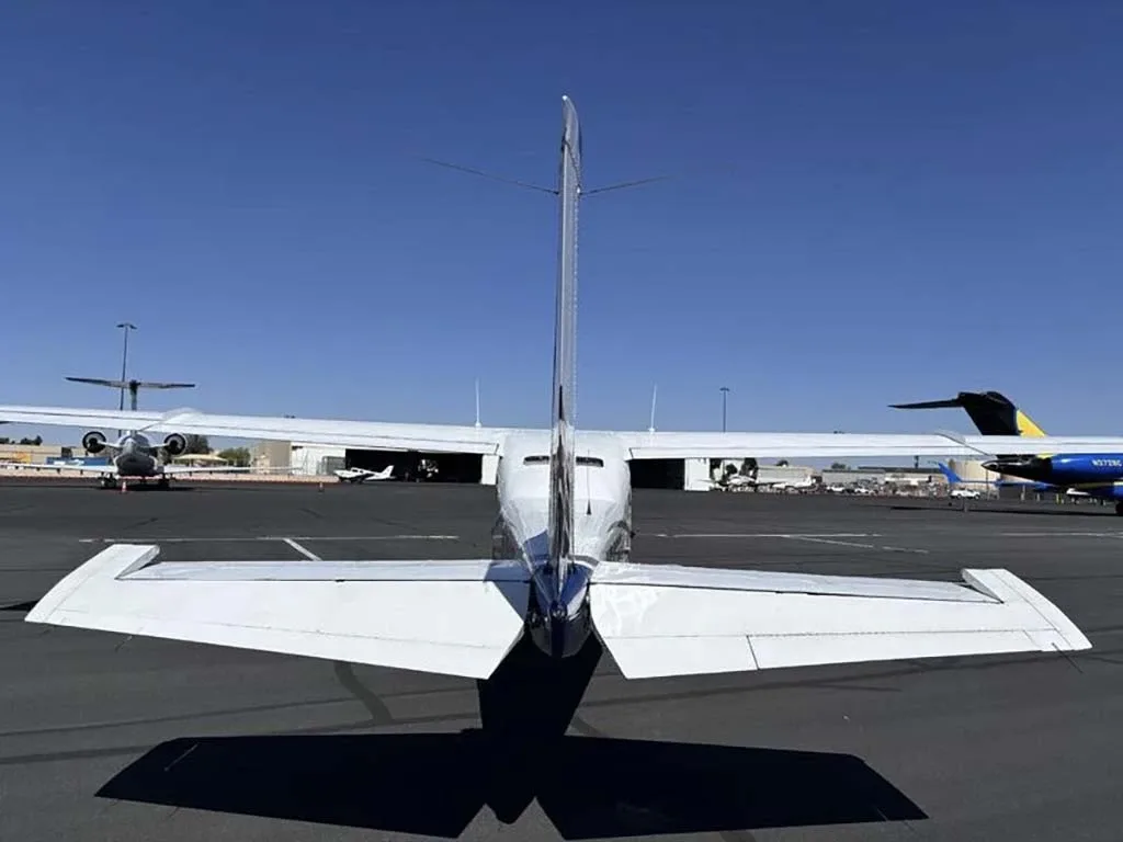 A rear view of the white and blue Cessna 210 Centurion with registration N66TE parked on an airfield.