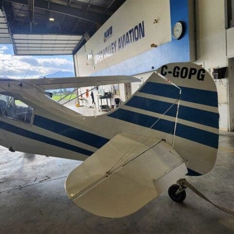 Tail section of a white and blue aircraft with registration C-GOPG inside a hangar.