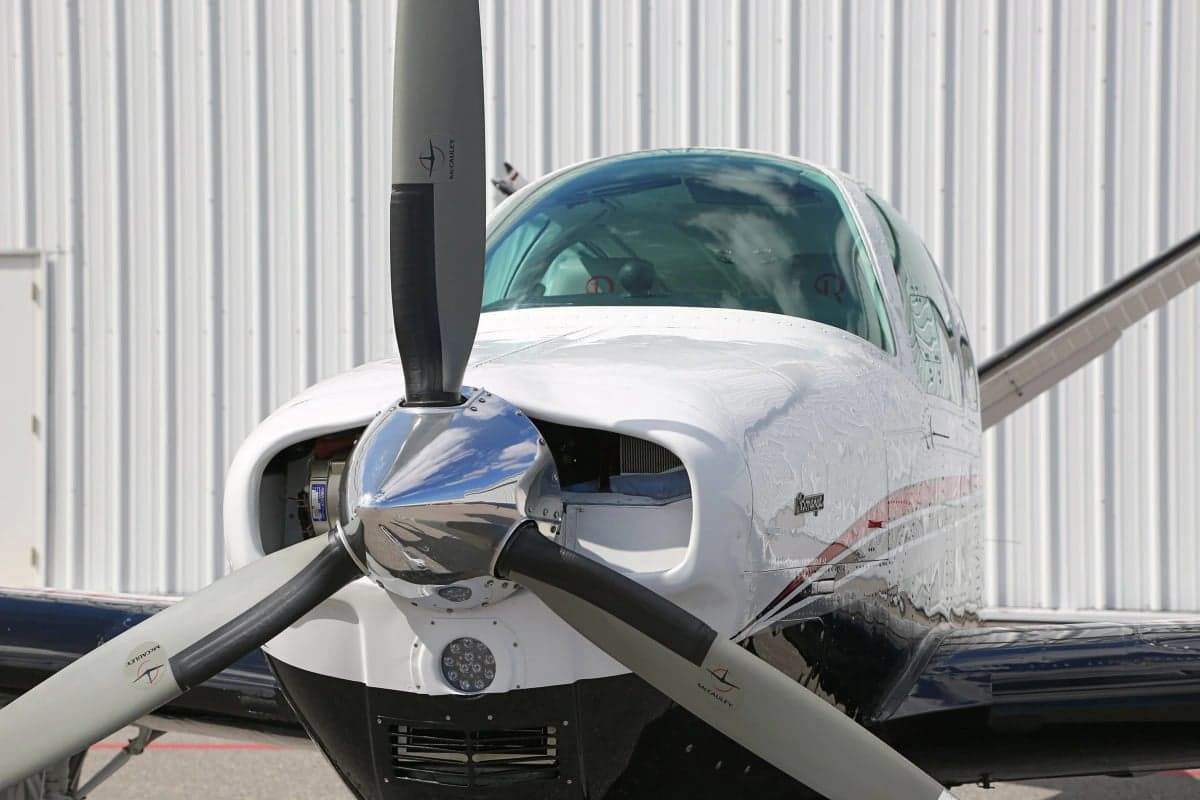 Close-up front view of a Beechcraft Bonanza aircraft on the ground in front of a hangar.