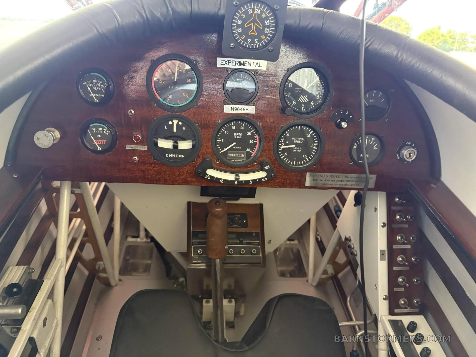 The cockpit of a biplane features a wooden instrument panel with analog gauges and a central control stick.
