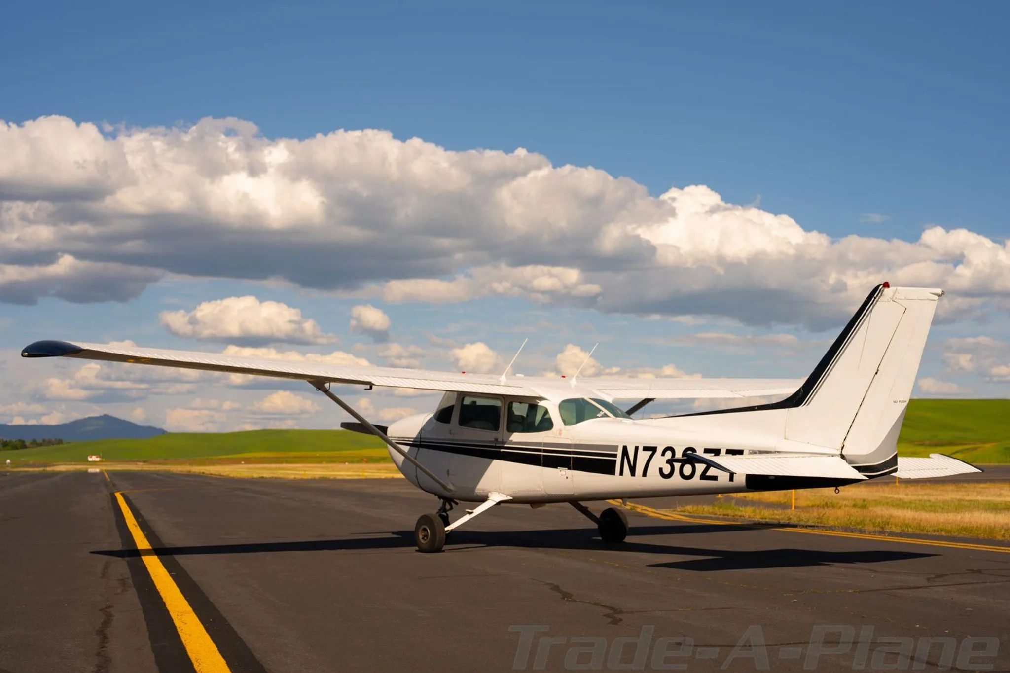 A white Cessna 172 with black stripes, tail number N738ZT, parked on an airfield with a clear blue sky.