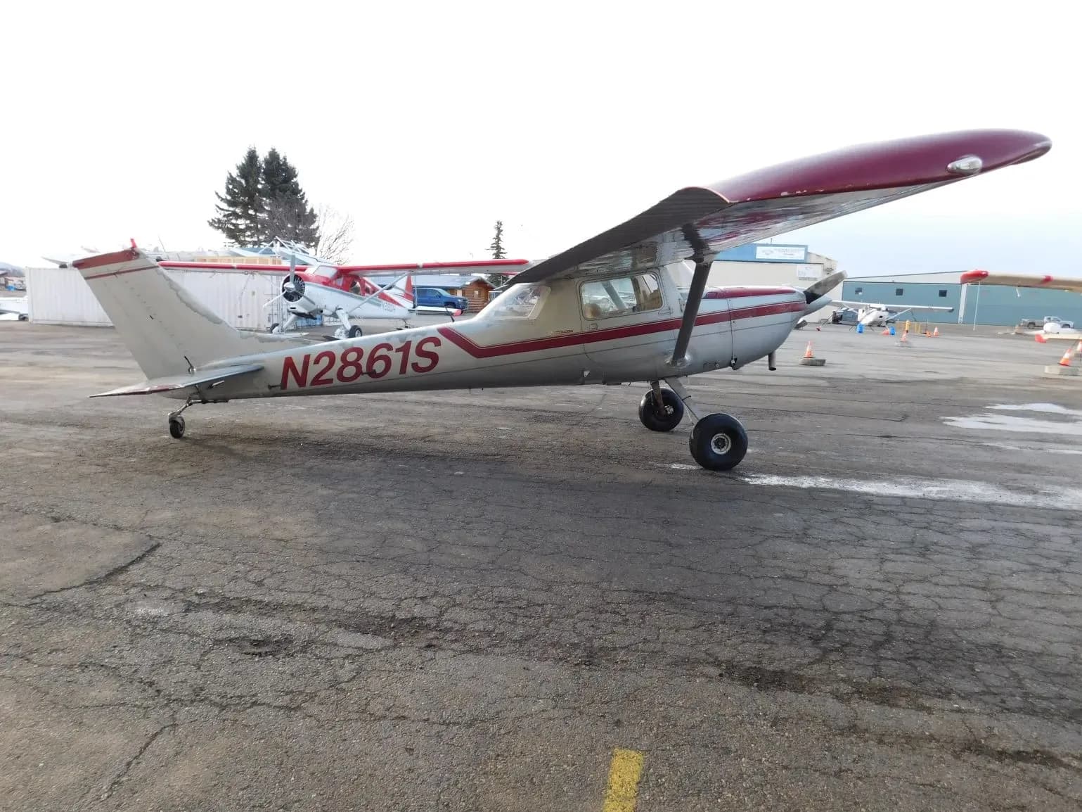 A silver and red single-engine propeller aircraft (N2861S) parked on a tarmac with other aircraft in the background.