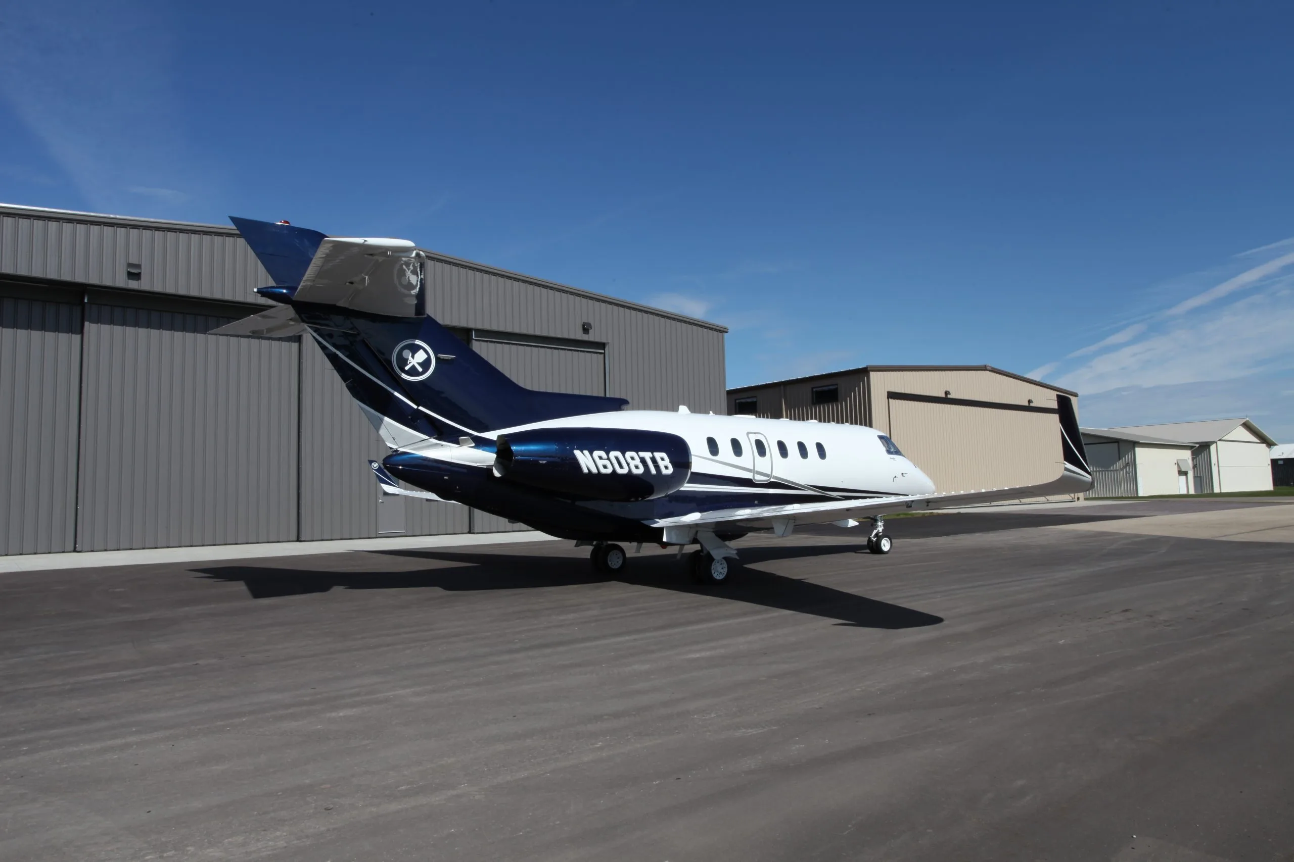 A Hawker 400XP aircraft is parked on the tarmac in front of a hangar on a sunny day.