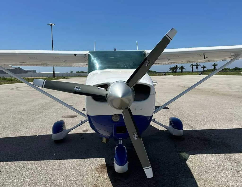 A head-on view of a blue and white Cessna 172 Skyhawk aircraft with its propeller centered.