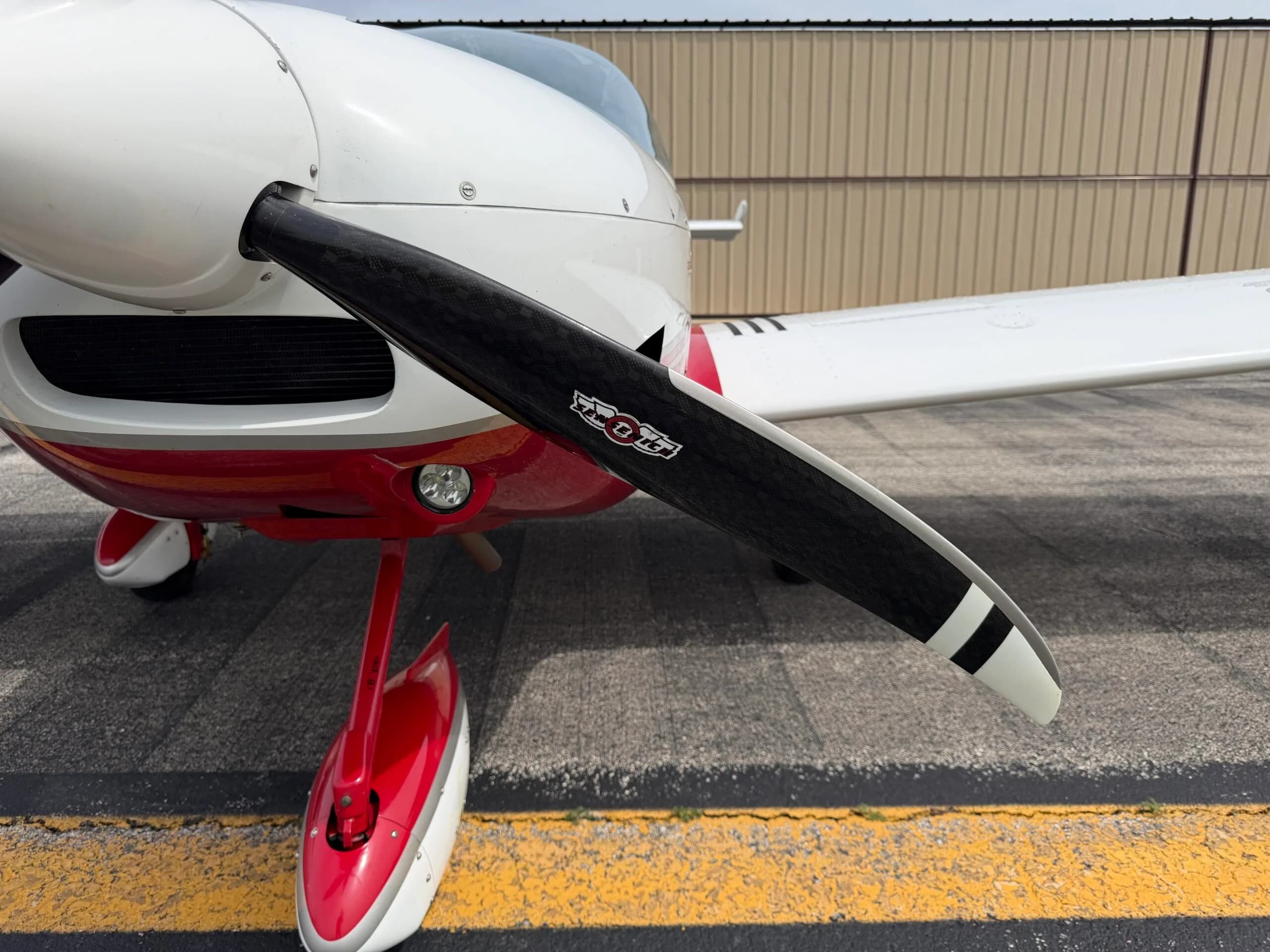 Close-up of the propeller and red and white nose landing gear of the SportCruiser aircraft, showing the 'Sensenich' logo on the blade.