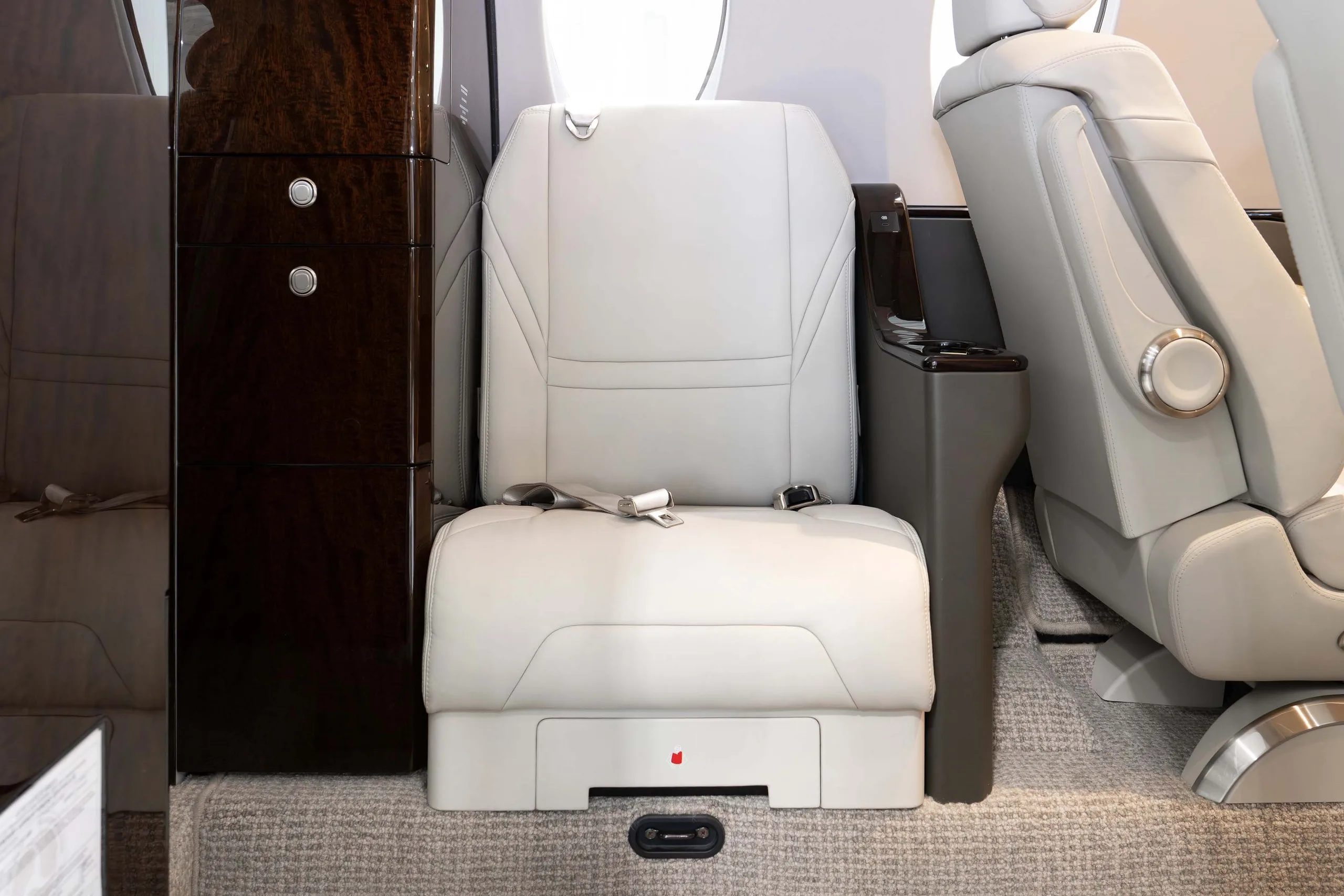 A close-up of a light grey leather seat in the business jet's cabin, next to dark wood cabinetry.