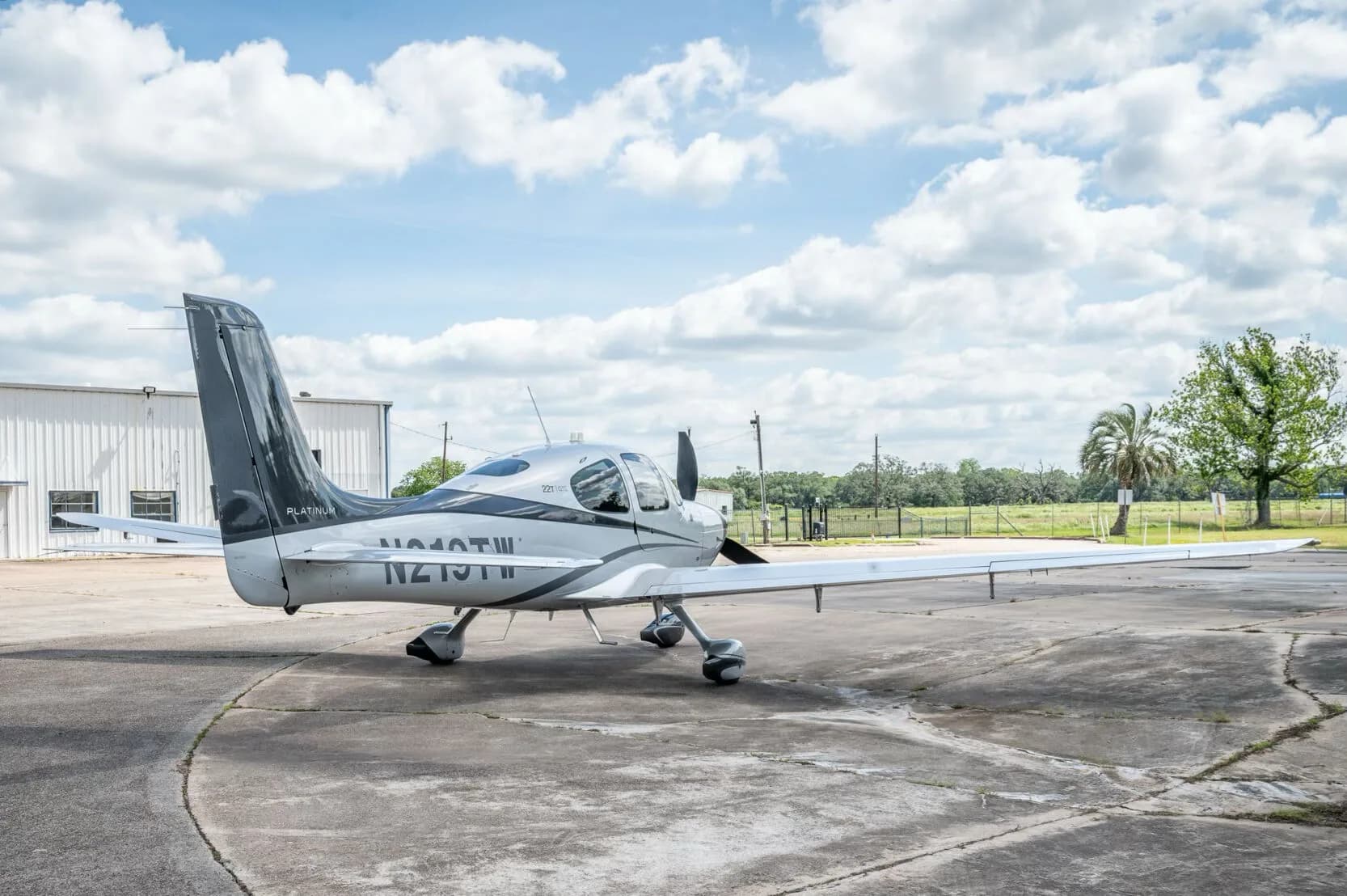 A rear-side view of the Cirrus SR22T GTS Platinum aircraft N219TW with a hangar and palm tree in the background.