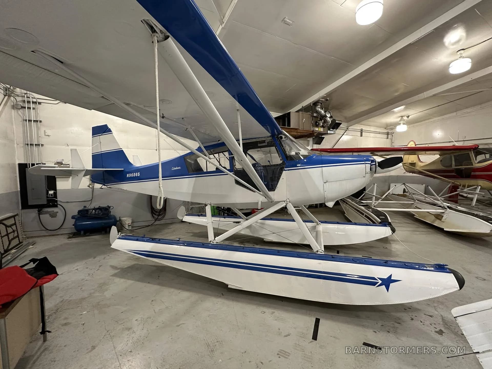 A blue and white Citabria floatplane with registration N9686S is parked in a hangar, viewed from the right side.
