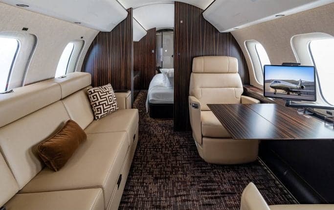Aircraft interior with a table, seats, and a monitor displaying an aircraft image.