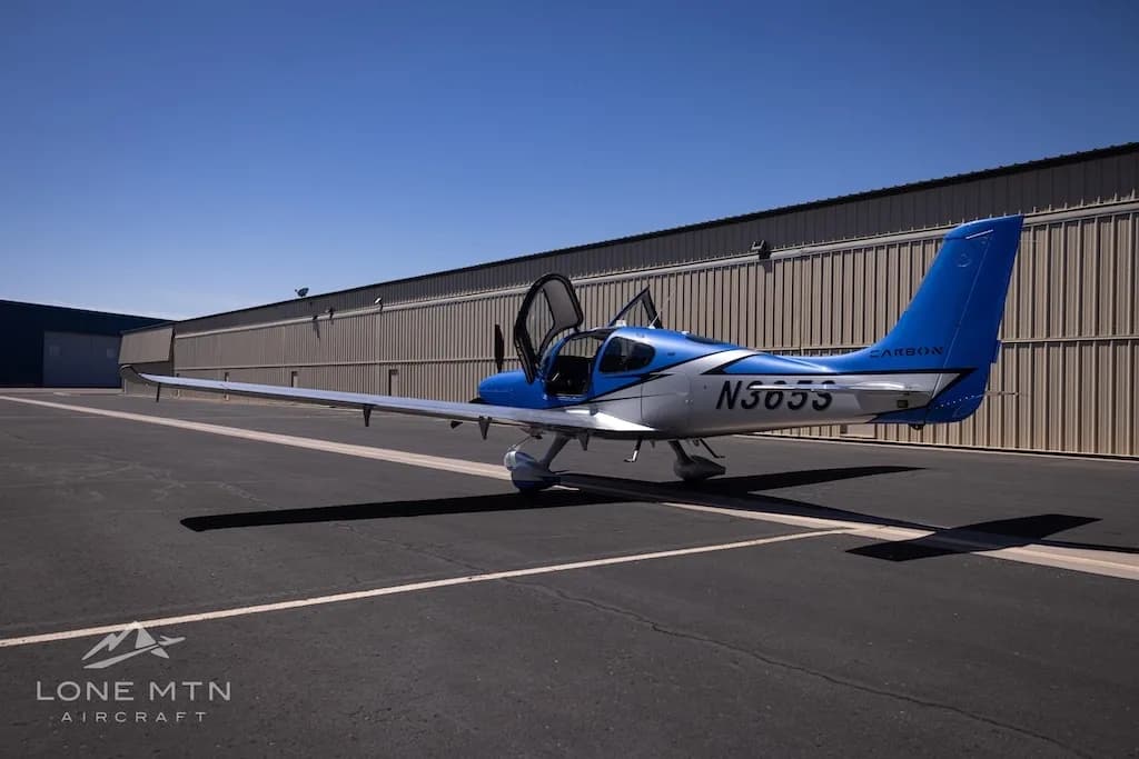 A rear three-quarter view of the blue and silver Cirrus SR22 aircraft, N365S, with its doors open, parked on an asphalt ramp.
