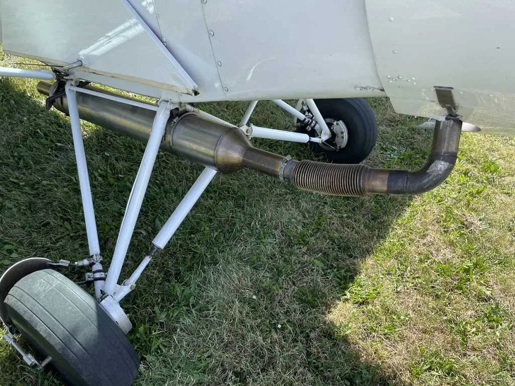 A close-up view of the aircraft's exhaust pipe and landing gear assembly on a grassy surface.