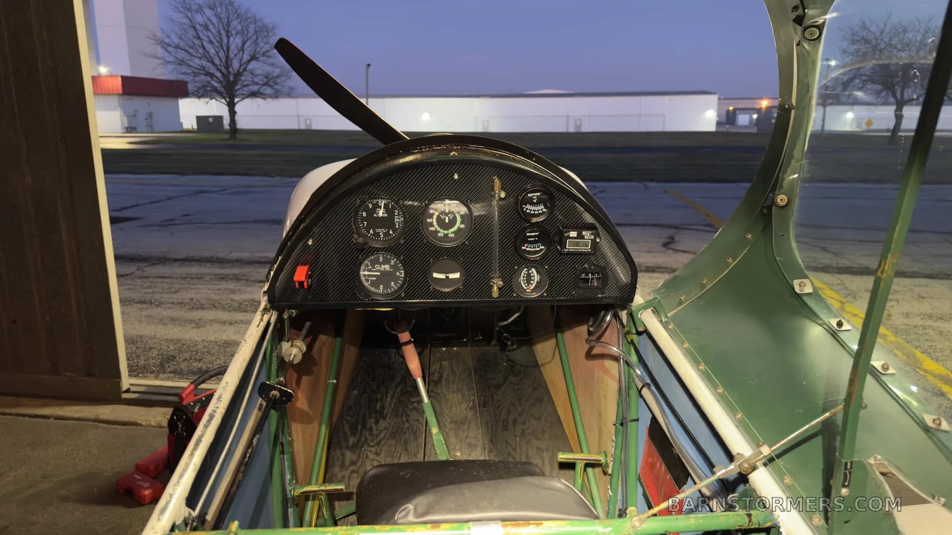 The cockpit of an experimental aircraft with a carbon fiber instrument panel and a view of the runway outside at dusk.