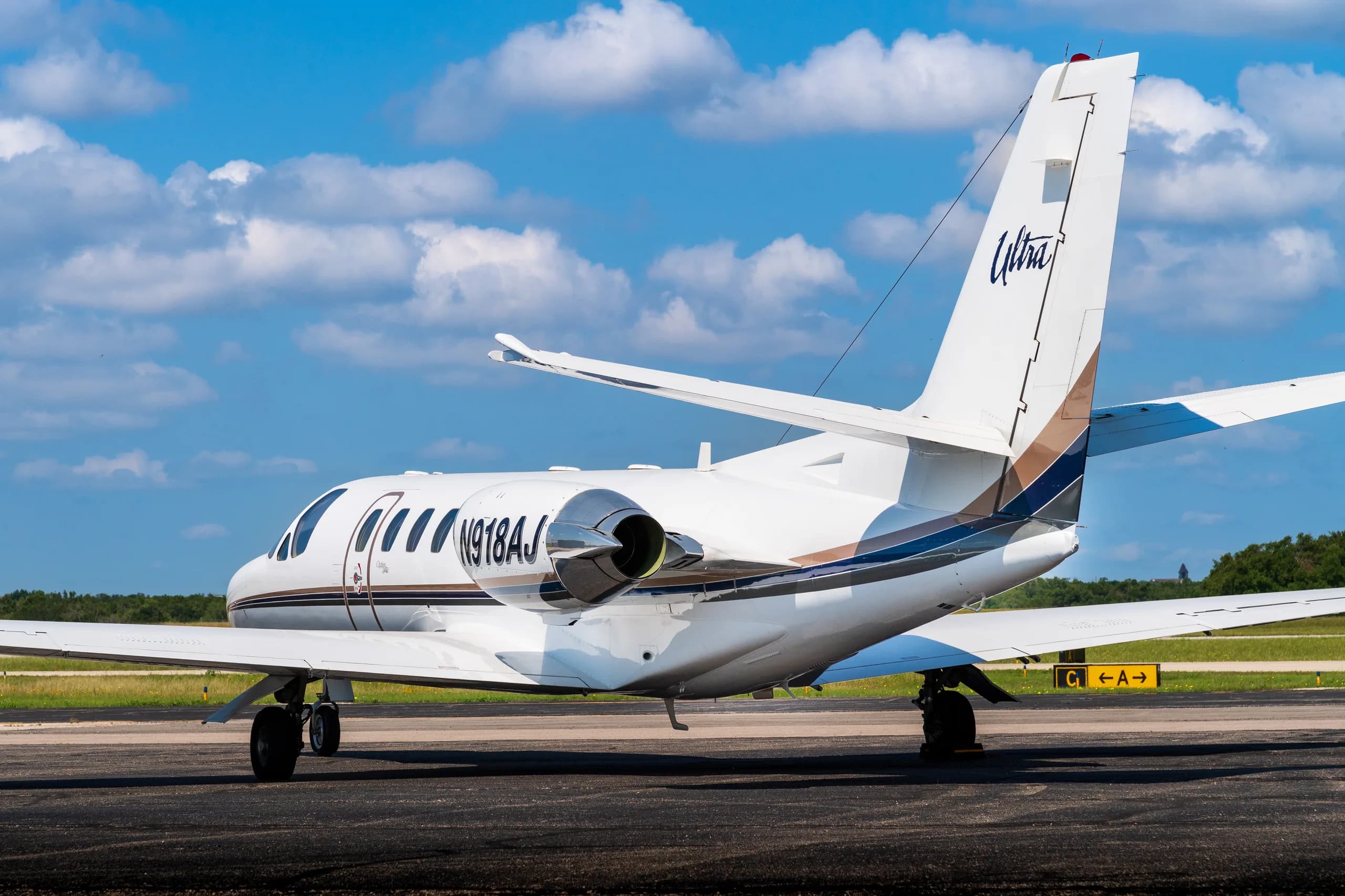 Rear view of a white Cessna Citation Ultra business jet, registration N918AJ, with blue and brown accent stripes, parked on an airfield.