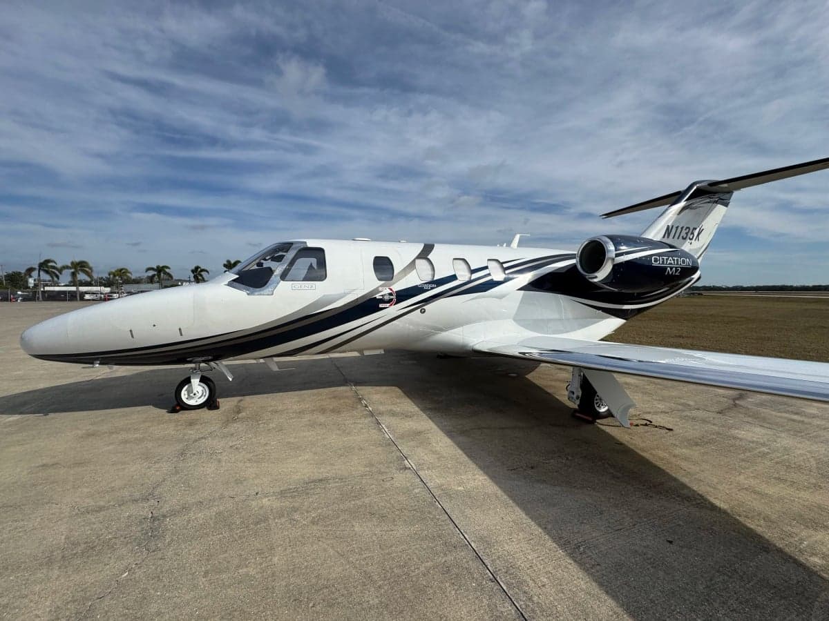 Side view of a Citation M2 jet with a white and dark blue paint scheme on the tarmac.