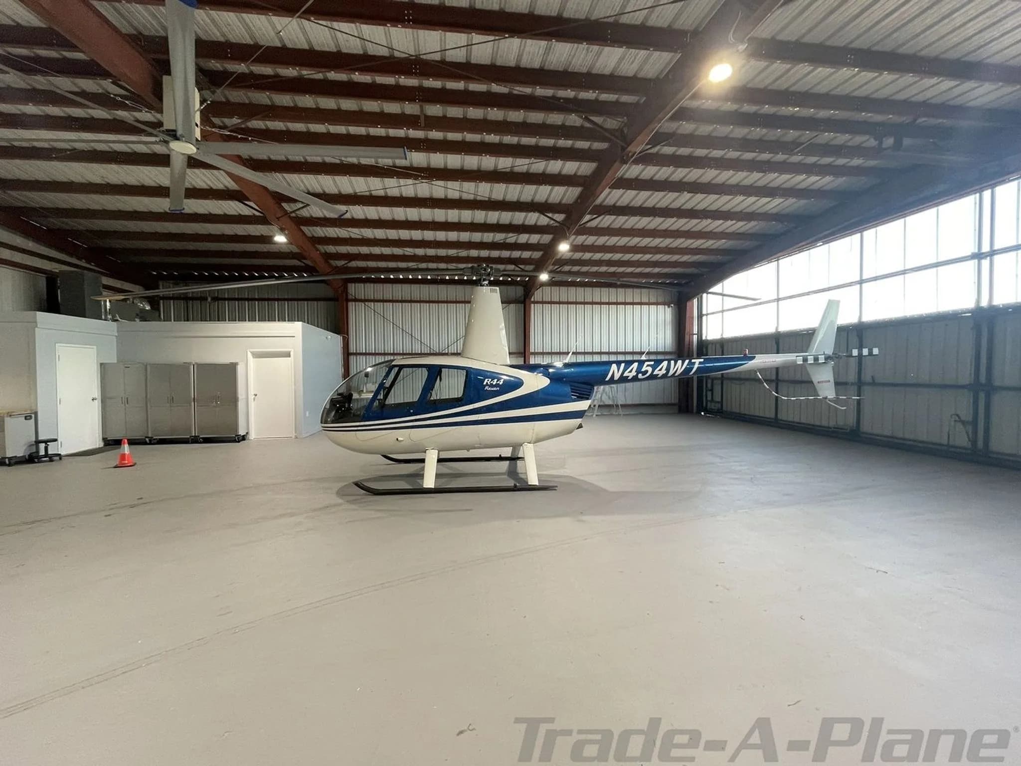 A blue and white Robinson R44 Raven helicopter with registration N454WT is parked inside a hangar.