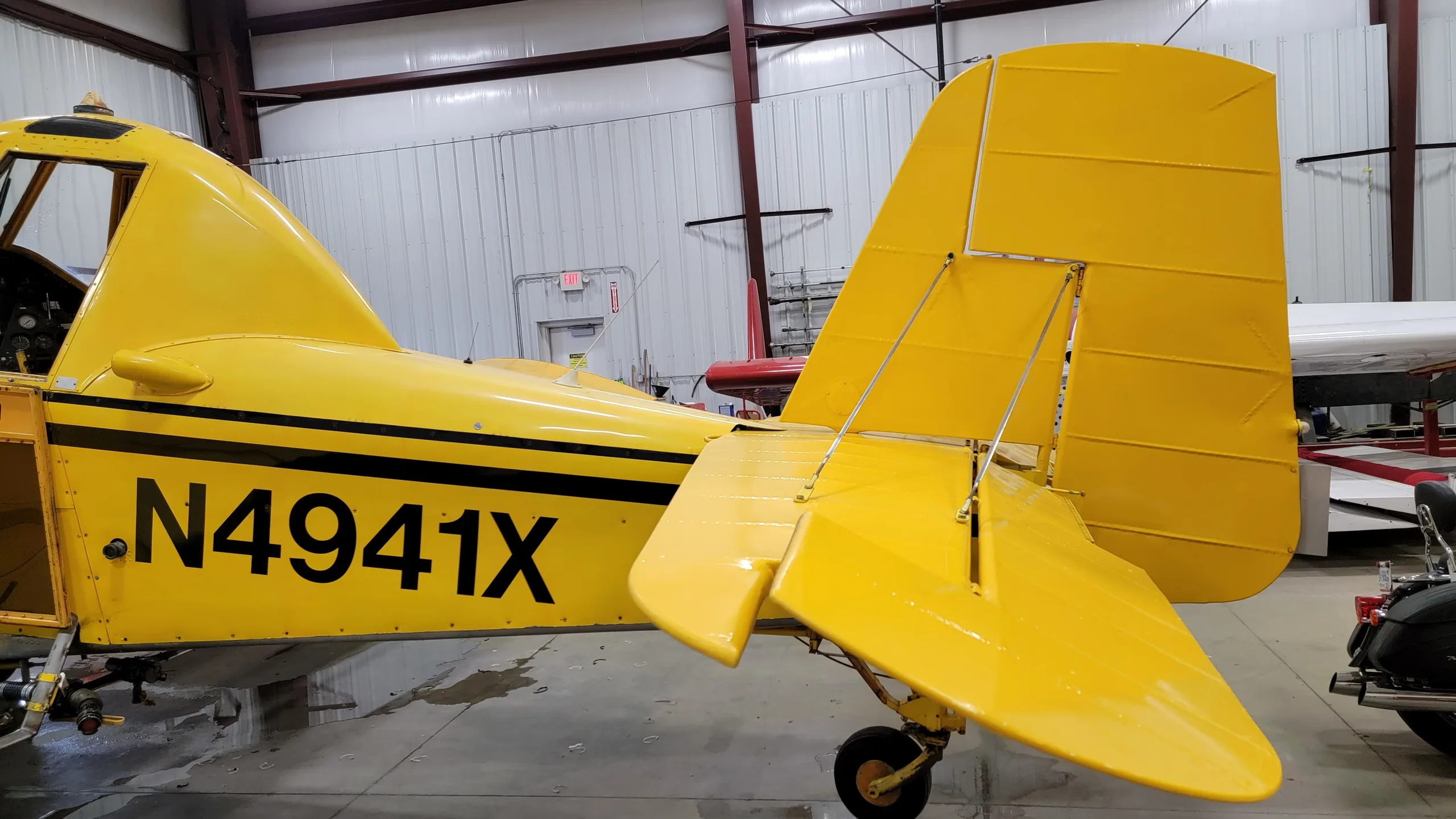 A rear-side view of the yellow aircraft, N4941X, showing its tail and registration number inside a hangar.