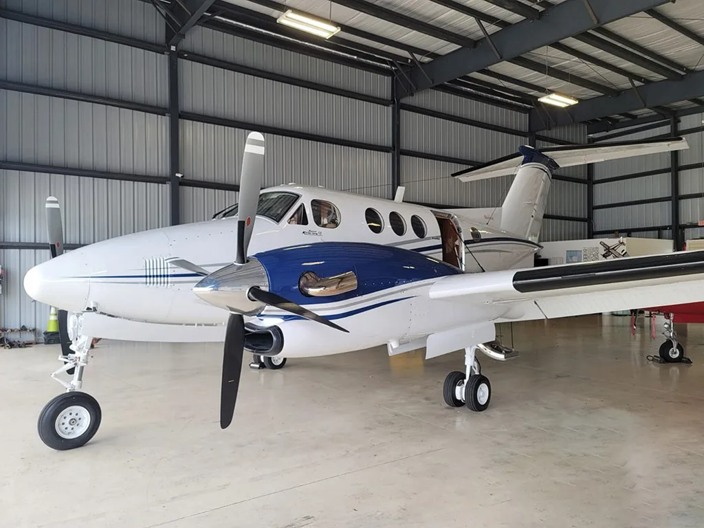 A white and blue twin-engine turboprop aircraft parked inside a metal hangar.