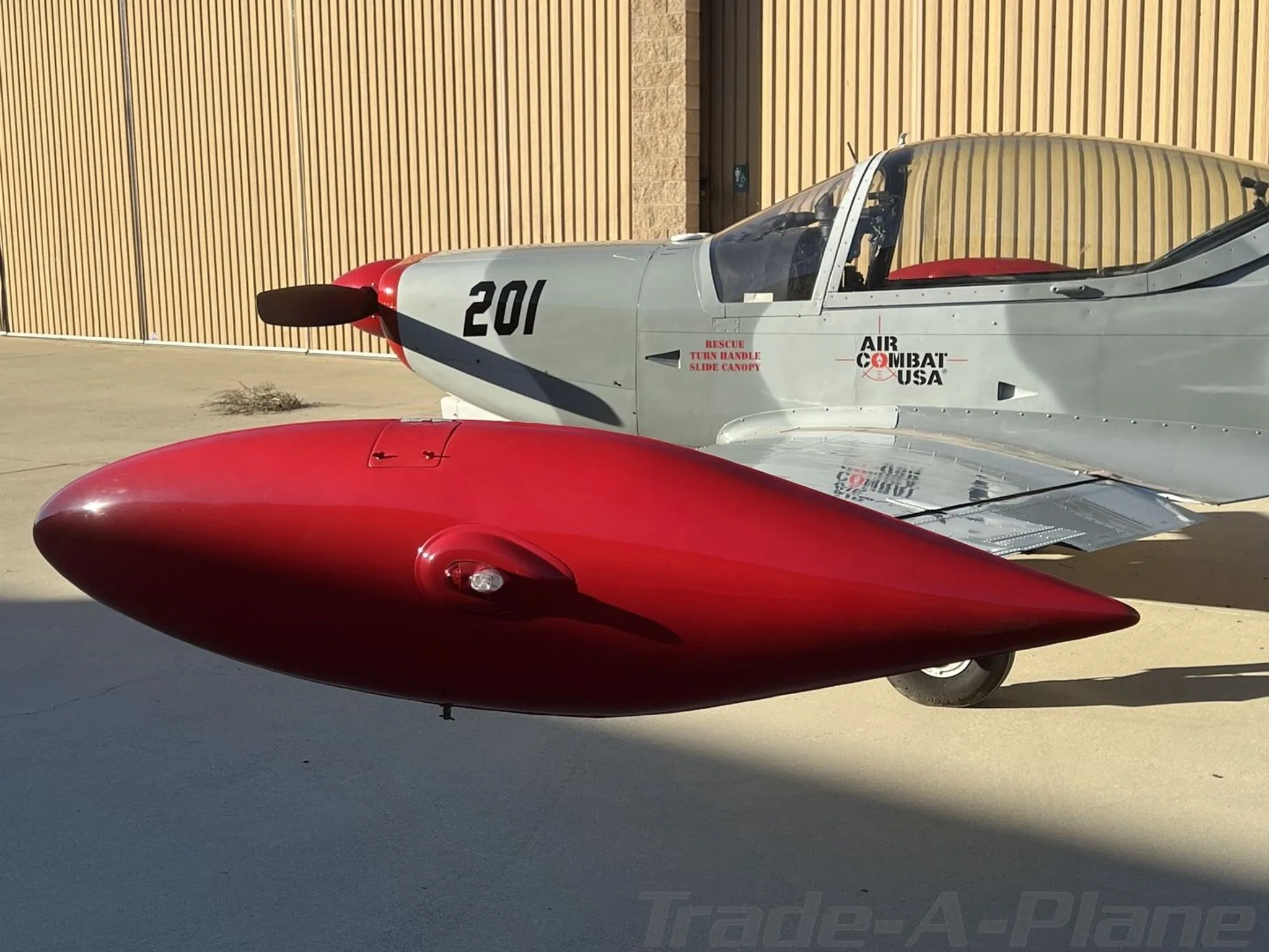 A close-up of the aircraft's nose, propeller, and a red external fuel tank.