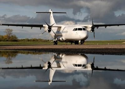 An ATR 42 aircraft parked on the tarmac with a reflection in a puddle.