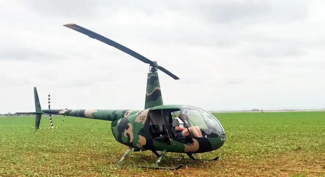 Robinson R-40 helicopter with camouflage paint scheme parked in a field.
