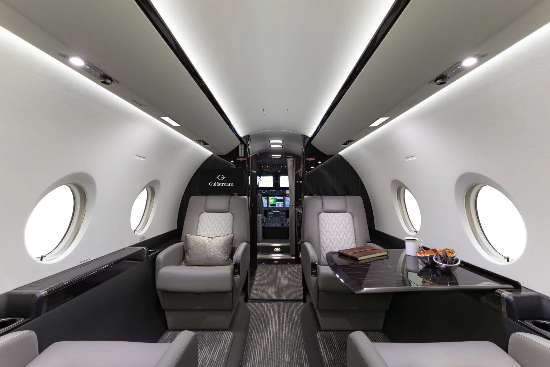 Forward view of the aircraft cabin with leather seats and oval windows, with tables extended.
