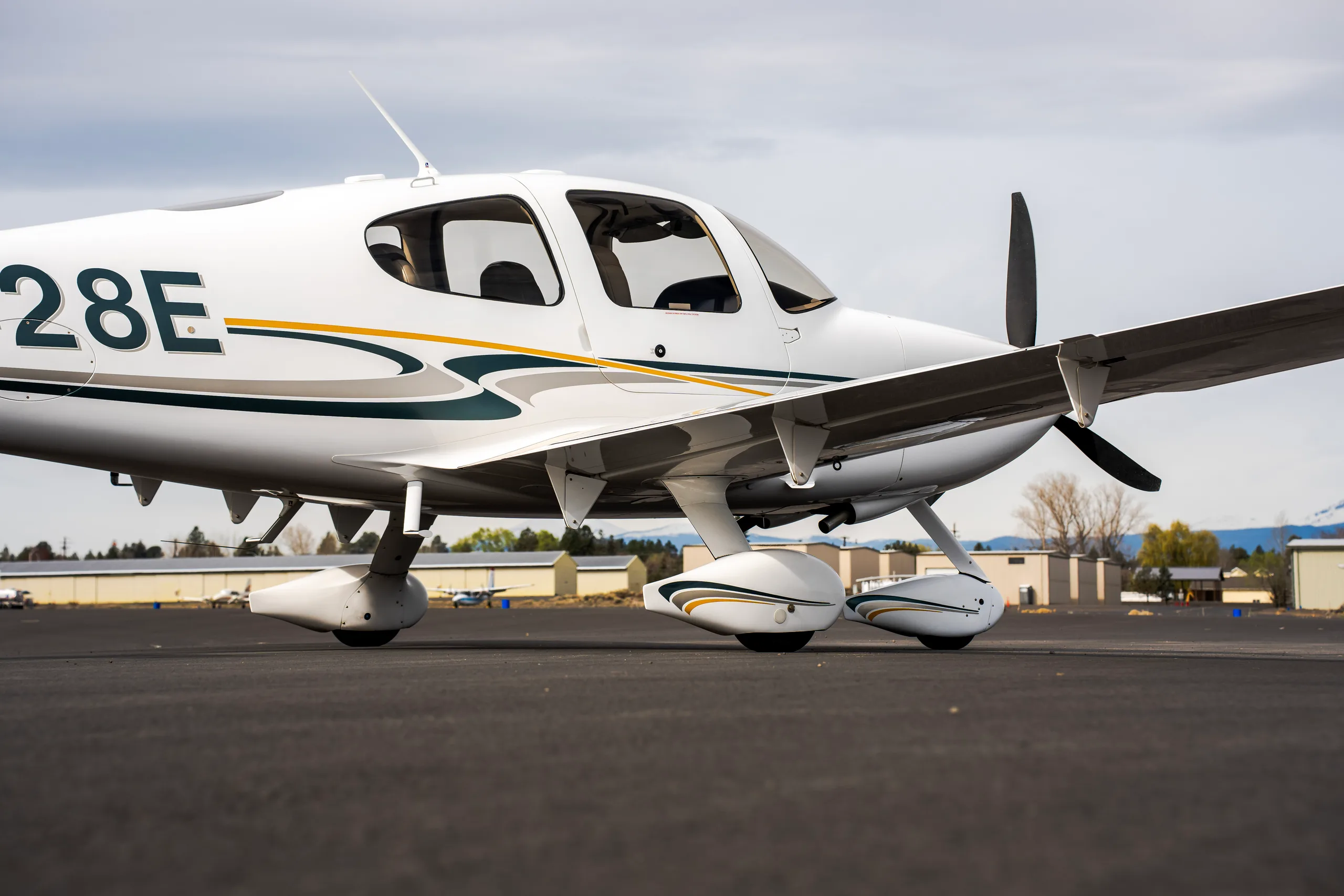 A close-up view of the front-right side of a white Cirrus SR22 aircraft, showing the propeller, landing gear, and tail number N2428E.