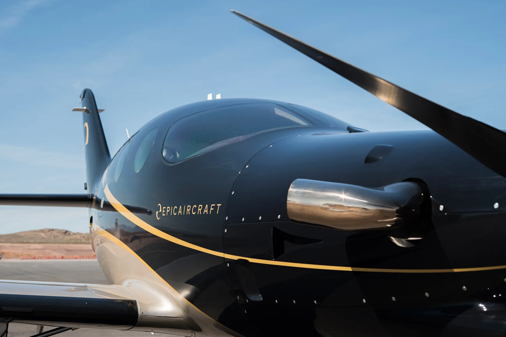 A close-up of the black and gold nose and propeller of the Epic E1000 GX aircraft.