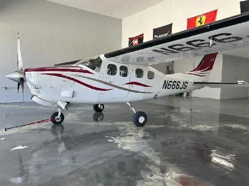 A Cessna 208 Caravan with a white and red paint scheme is parked in a hangar.