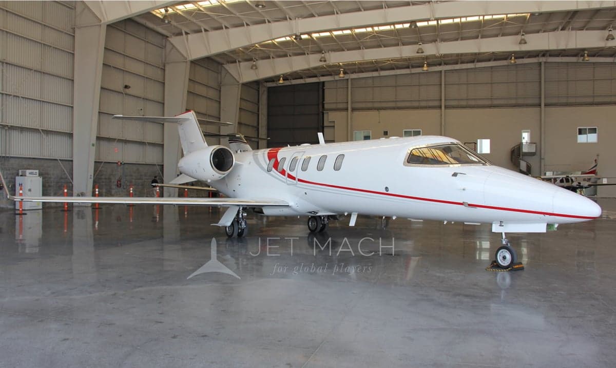 A white Learjet 75 with red and grey stripes parked inside a large hangar.