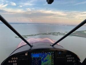 View from the cockpit of a Cubcrafters aircraft in flight over a body of water.