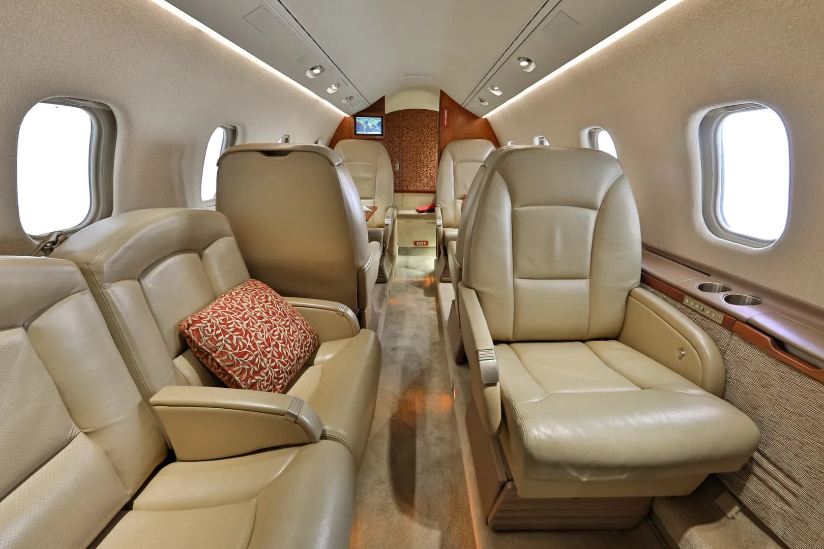 The elegant interior cabin of a business jet, featuring rows of beige leather seats and a red patterned pillow.