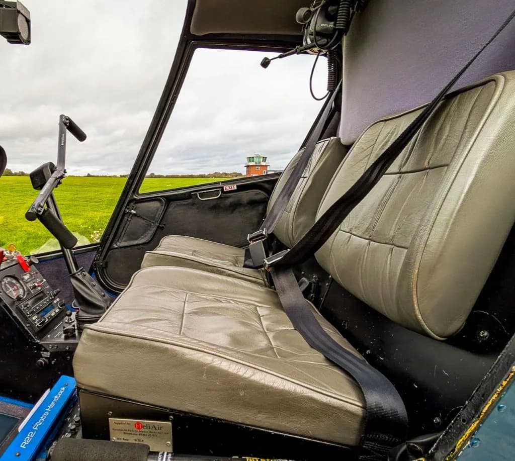The grey leather seats and interior cabin of a helicopter, with a control tower visible through the window.