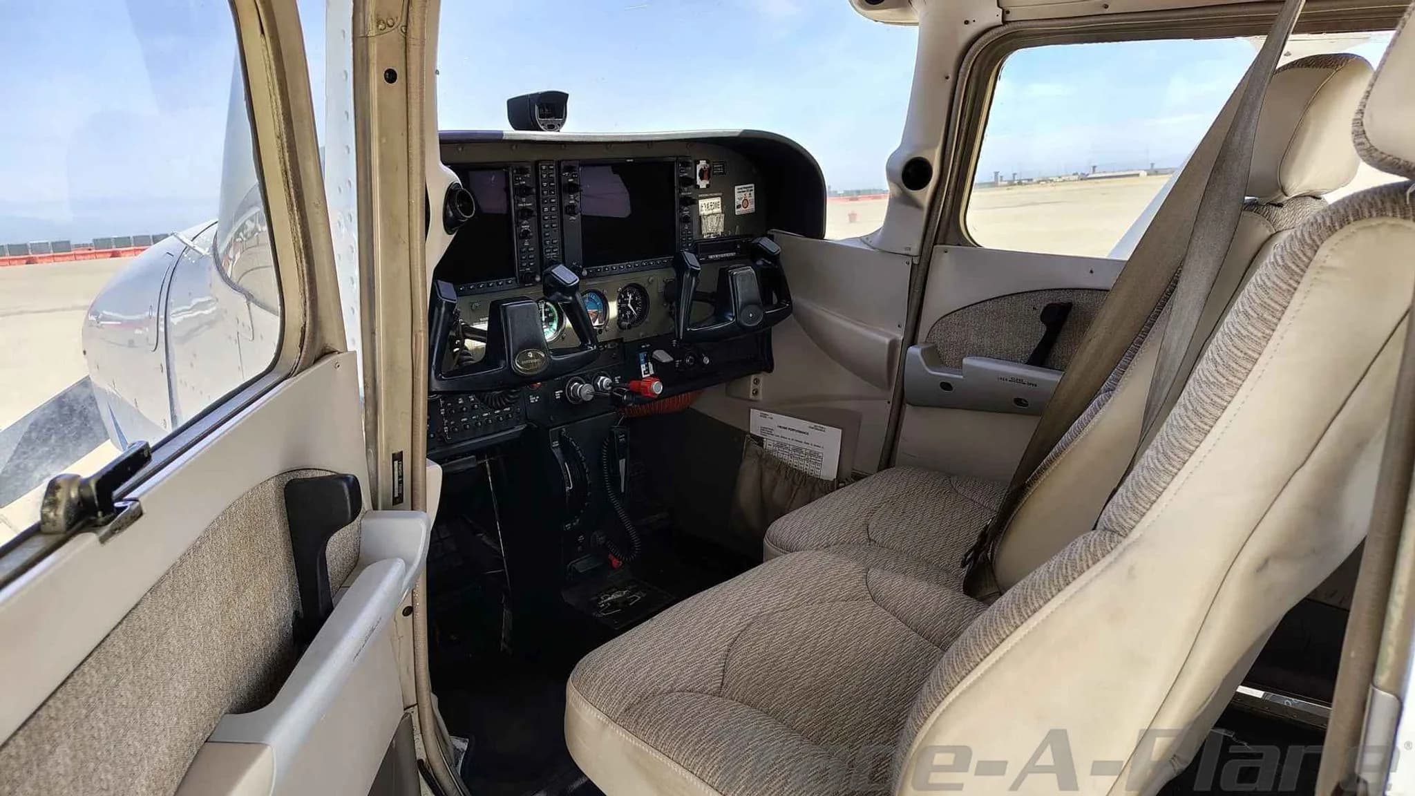 The aircraft's front cabin interior, showing the cockpit and two light-colored fabric seats.