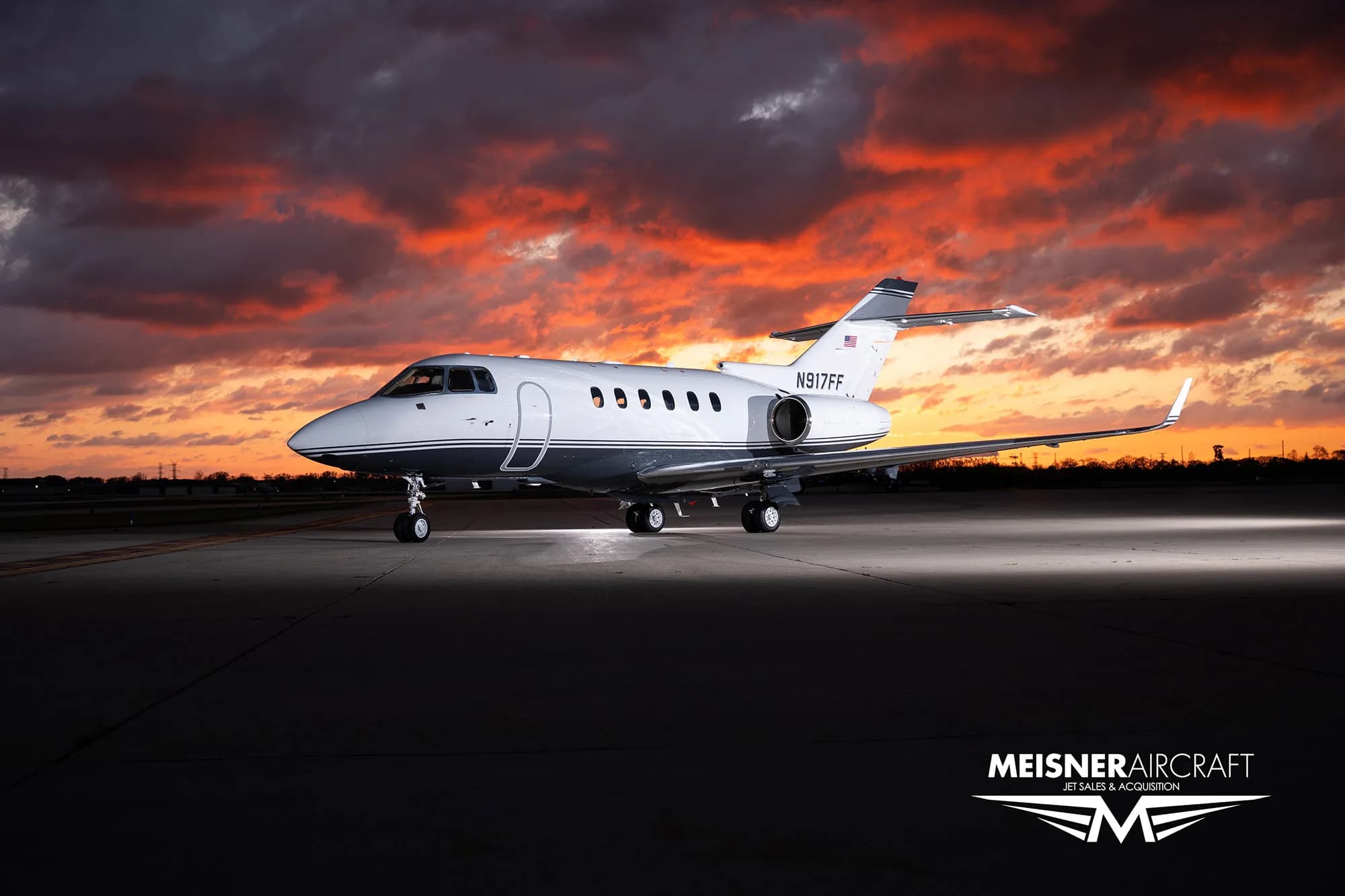 A white and grey business jet (N917FF) parked on a tarmac at sunset.