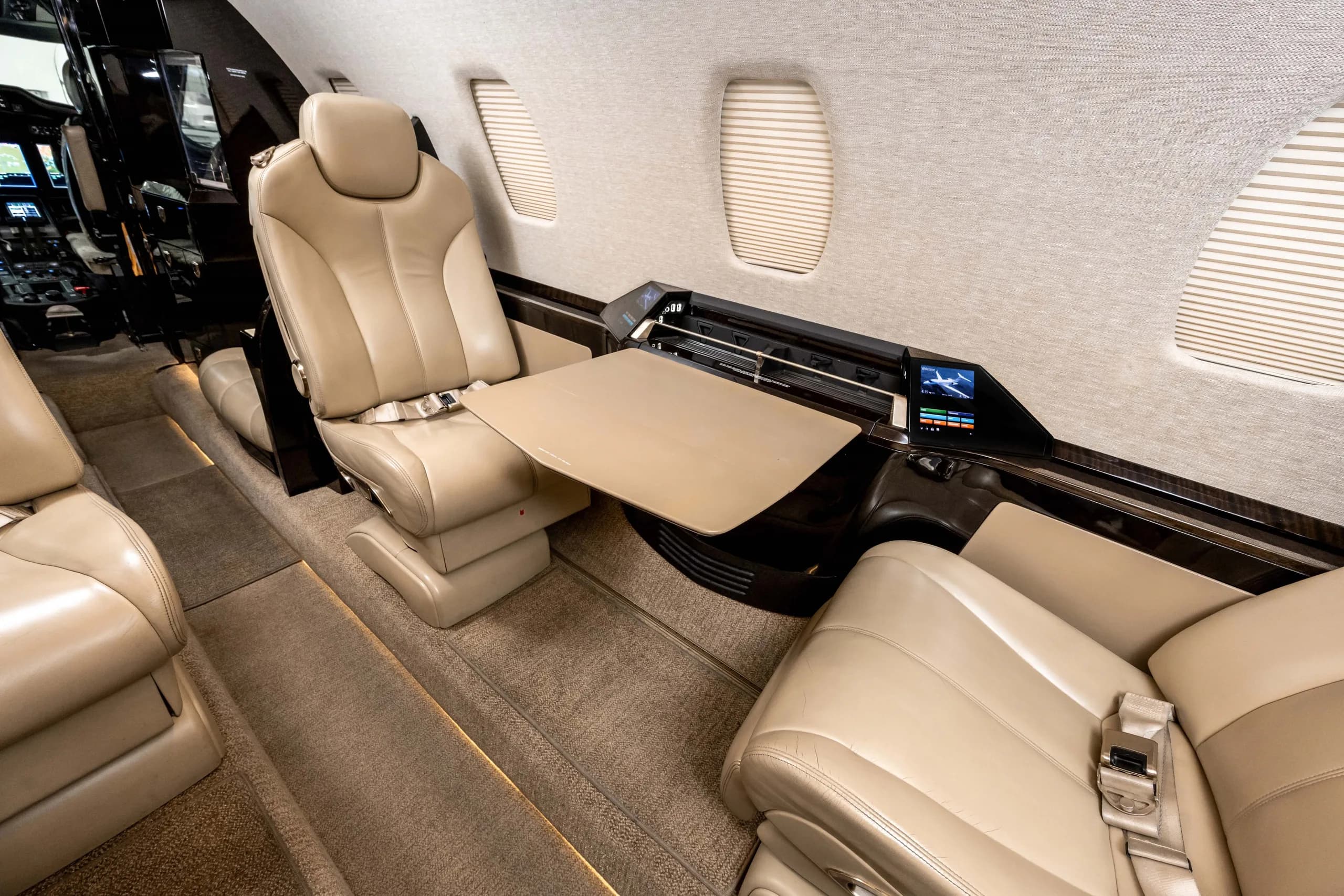A close-up view of two light tan leather seats in a business jet cabin, with a fold-out table extended between them.