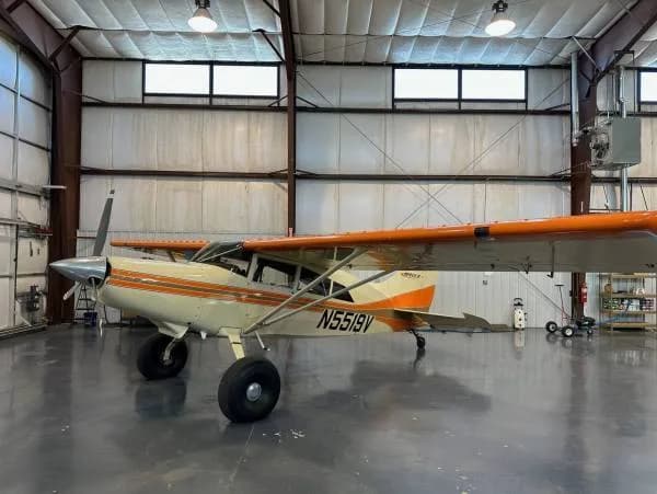 A Maule aircraft with registration N5519V, painted white and orange, viewed from the left side in a hangar.