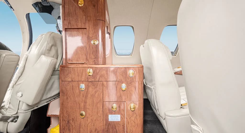 A close-up view of the aircraft's cabin showing a tall wooden cabinet with gold accents and light cream leather seats.