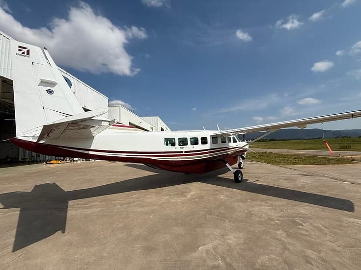 A maroon and white Cessna Caravan parked on the tarmac with a hangar in the background.