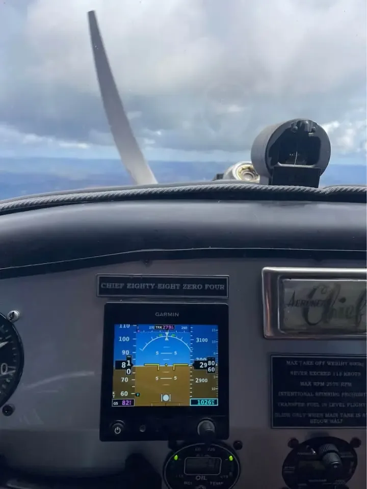 The cockpit instrument panel of an Aeronca Chief, featuring a Garmin display and other gauges, with a propeller visible outside.