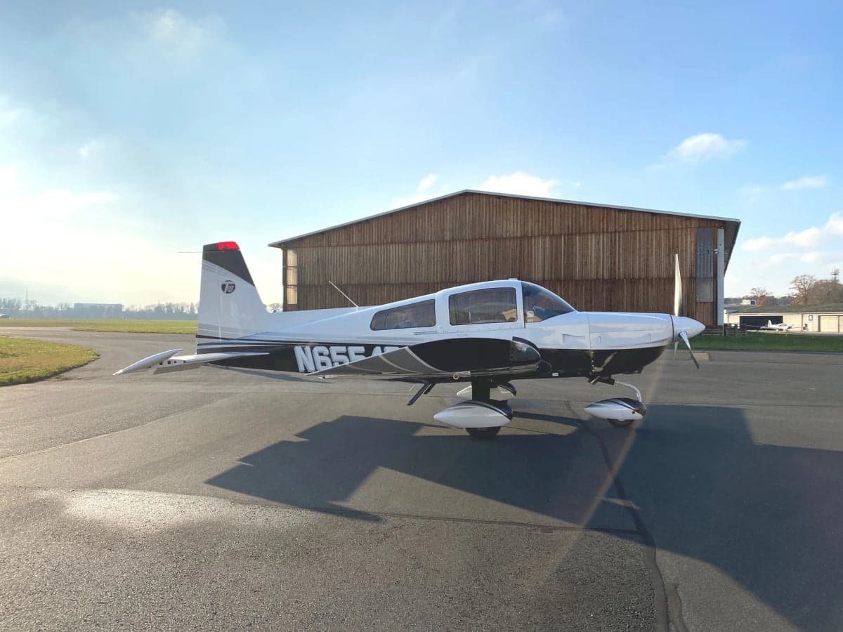A white and black aircraft sits on the tarmac under a blue sky.