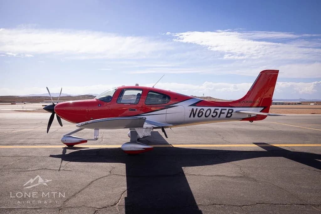 A side profile view of a red and silver Cirrus SR22T aircraft (N605FB) on an airfield under a bright sky.