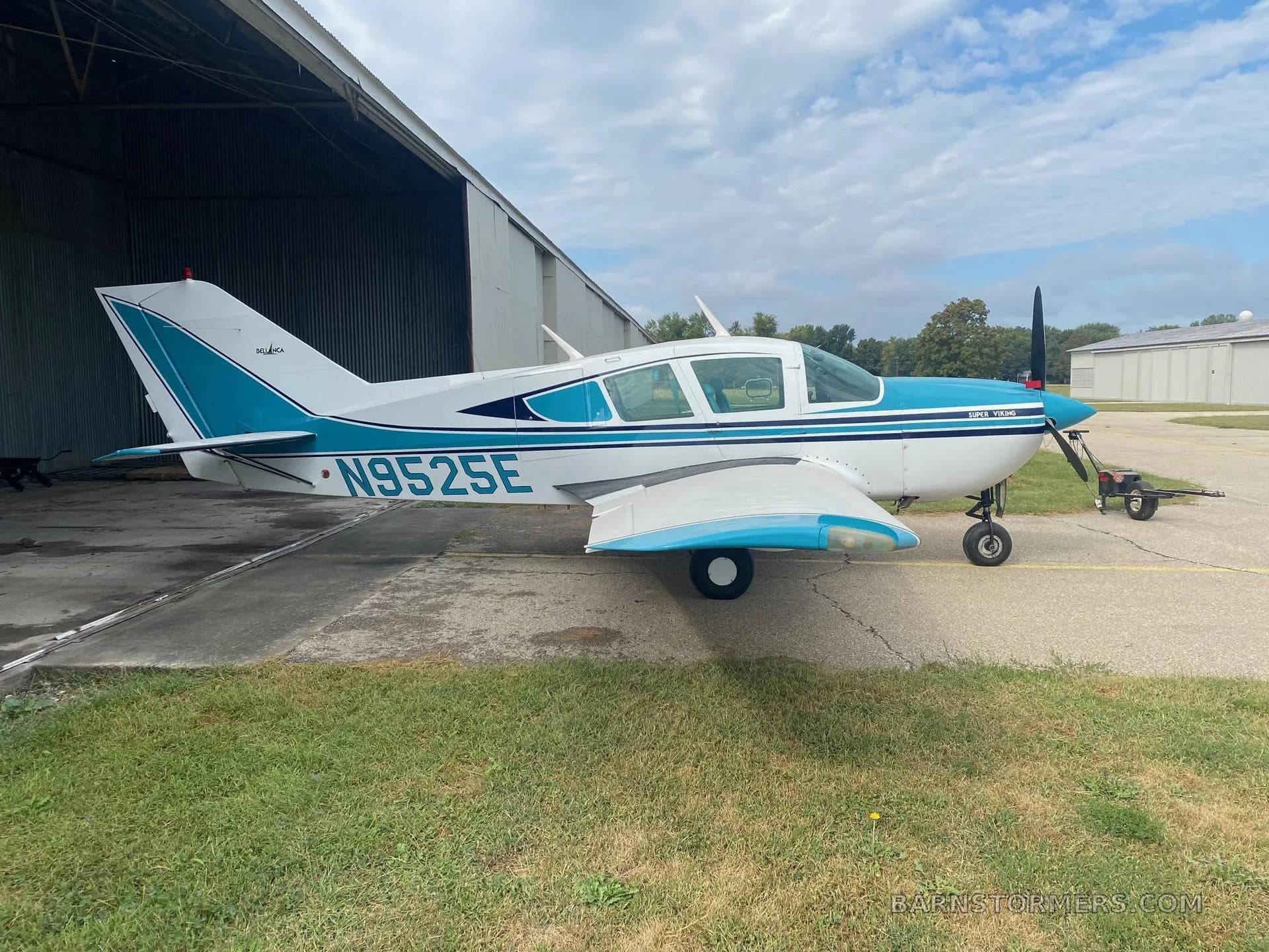 A Bellanca Super Viking aircraft (N9525E) with a white and blue paint scheme parked on an tarmac next to a hangar.