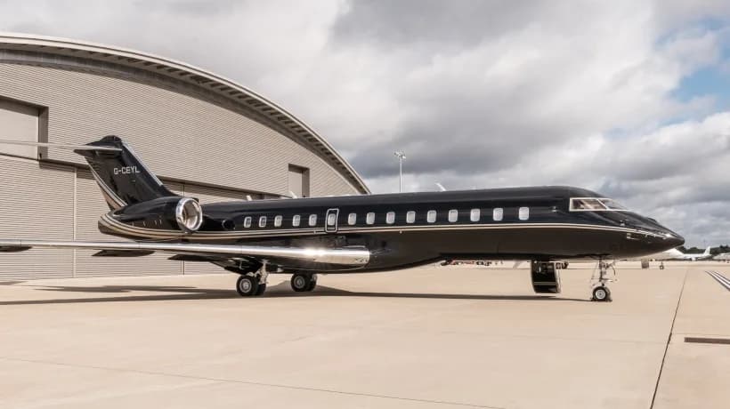 A black Bombardier Global business jet with gold accents parked on an airfield next to a modern hangar.
